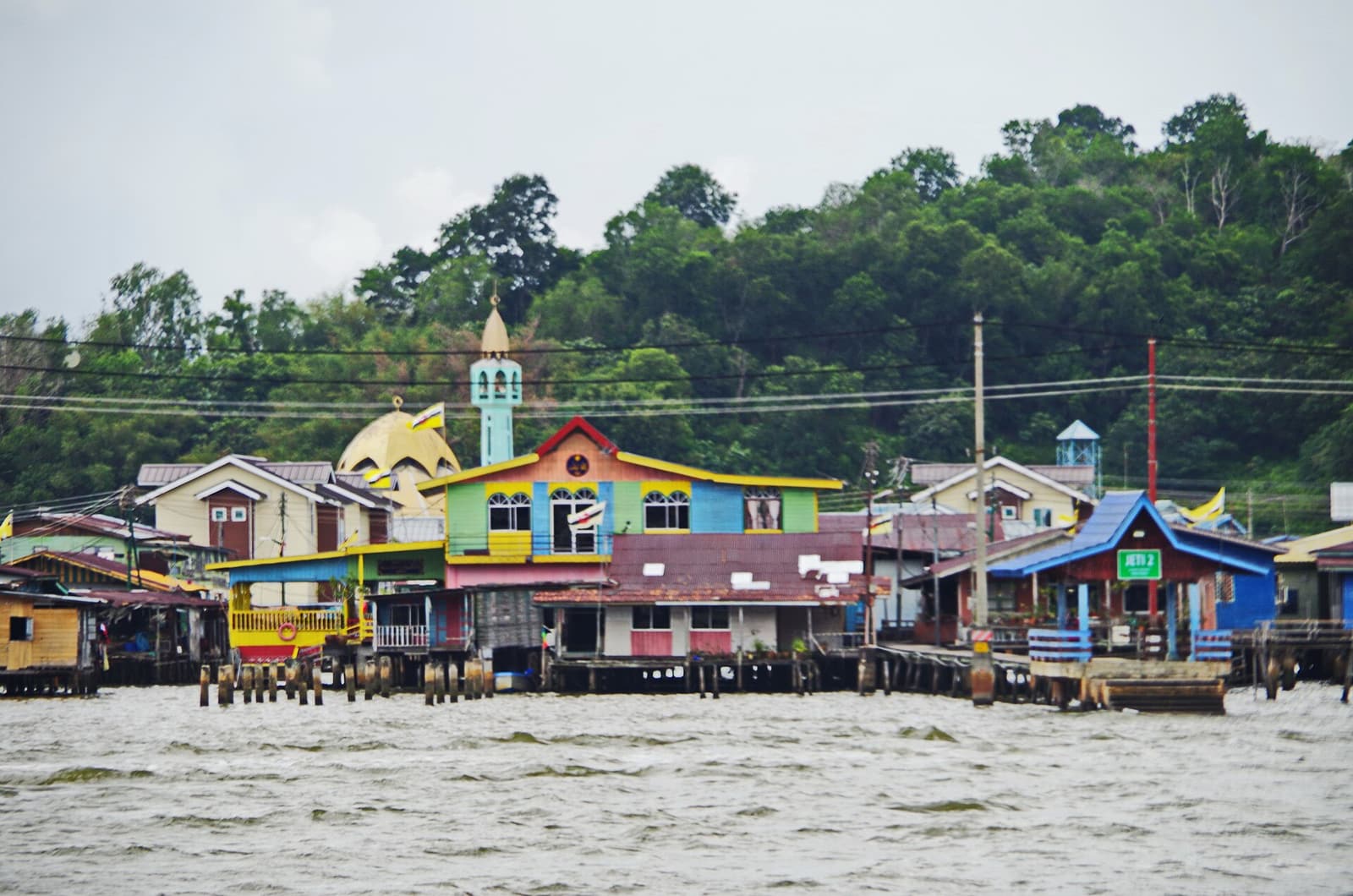Brightly painted stilt houses of Kampong Ayer below a forested hill