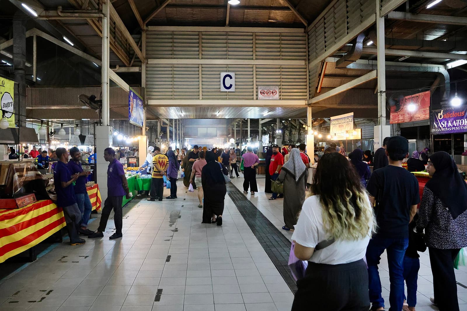 Shoppers walking between food stalls inside the covered Gadong night market