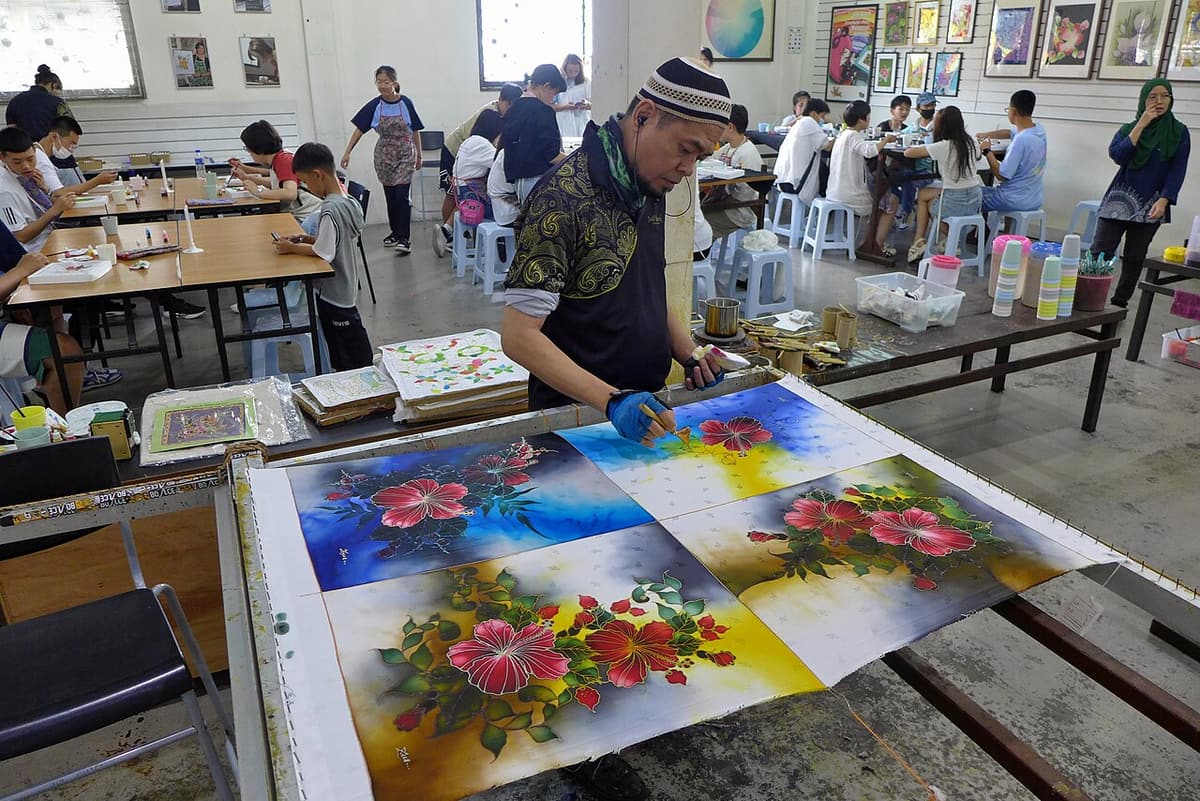 An instructor painting flowers on batik cloth in a workshop