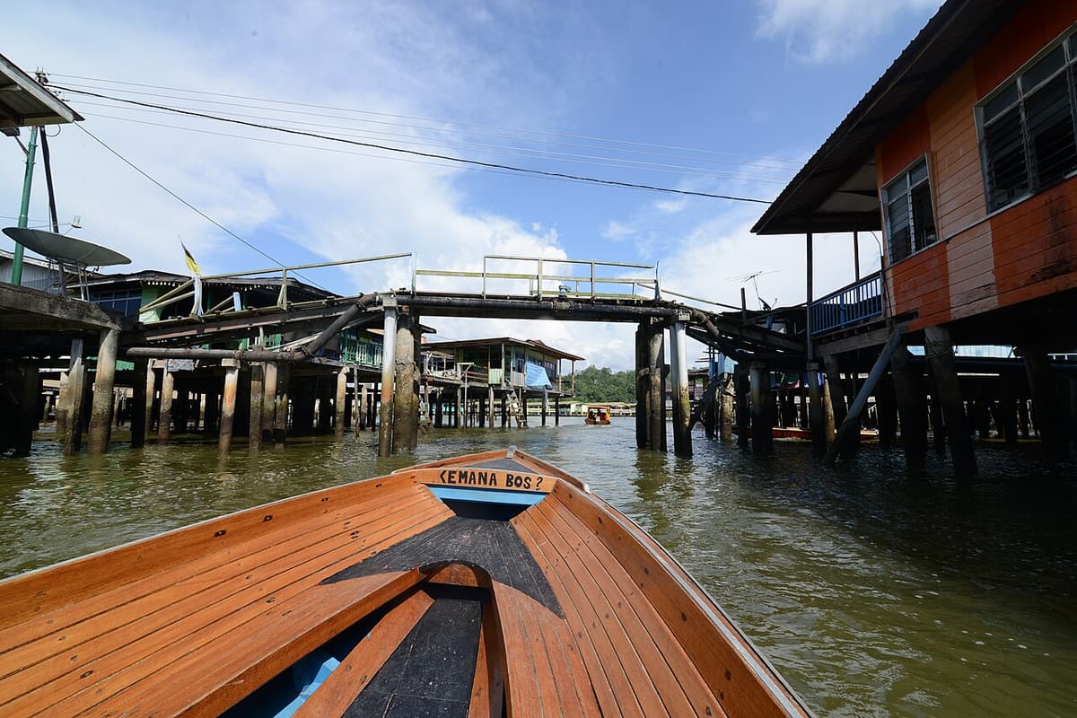 The bow of a wooden boat passing between stilt houses in Kampong Ayer