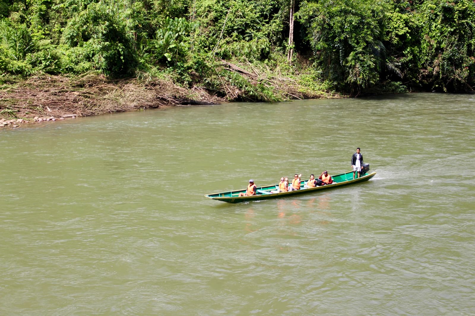 A longboat carrying passengers on a river between rainforest banks in Temburong